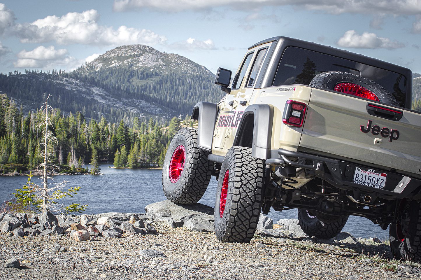 Jeep Gladiator customized with off-road tires and red wheels parked facing the lake.