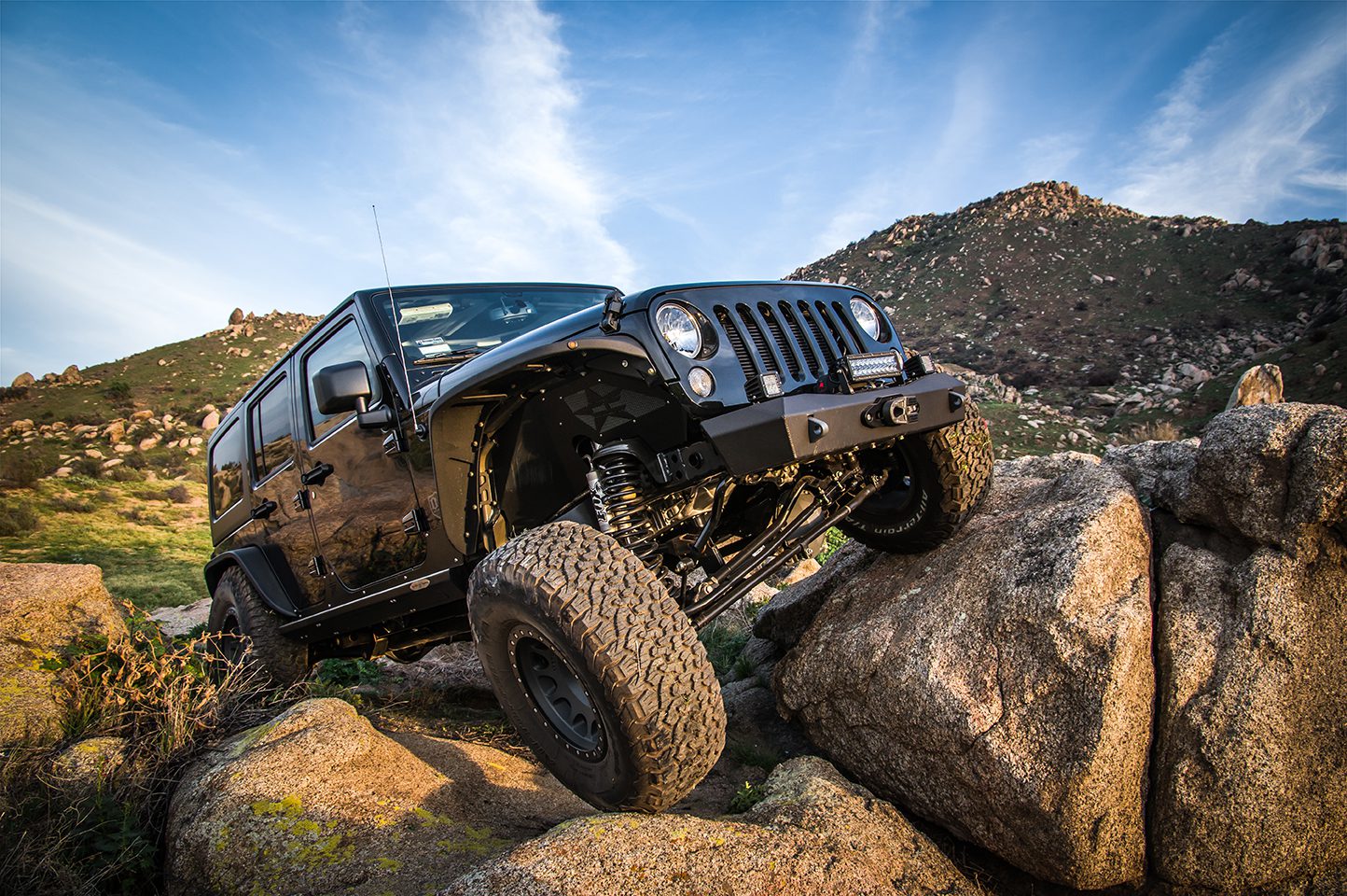 Jeep Wrangler parked on rocky mountain equipped with lifts and driver front wheel on a rock