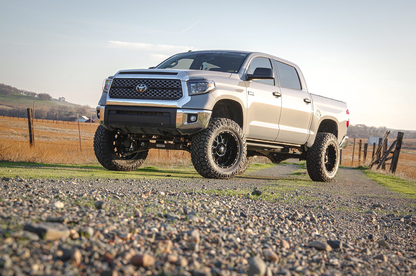 Gold Toyota Tundra parked on a sunlit road with rugged terrain in the background.