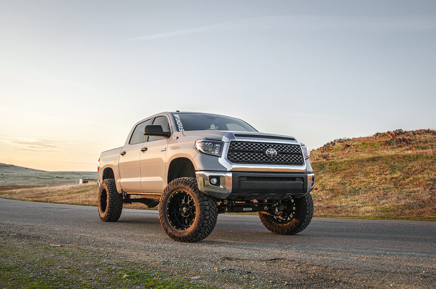 Gold Toyota Tundra parked on a scenic mountain overlook with expansive views of rugged terrain and a clear sky.
