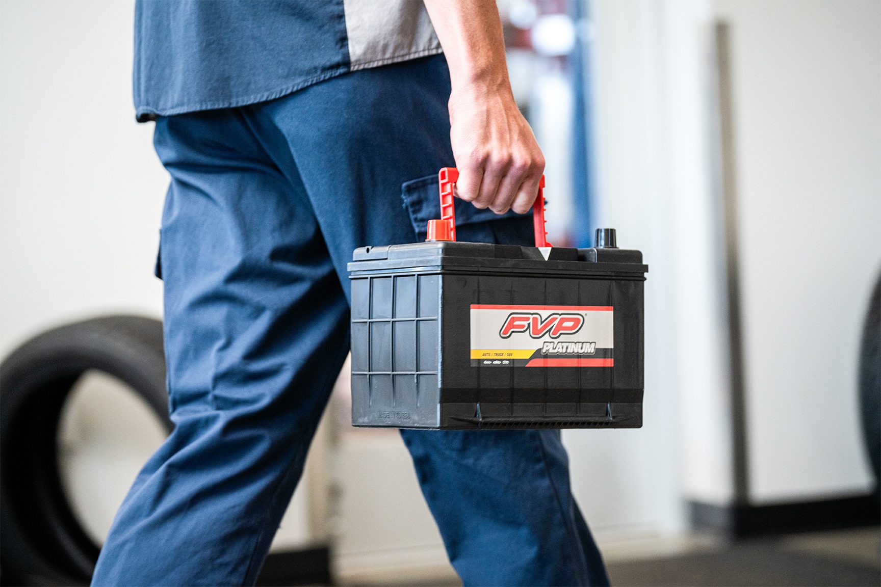 Burt Brothers technician walking with an FVP Platinum battery in a clean, well-lit service bay.
