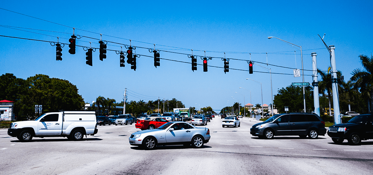 View from a wide, sunlit intersection with multiple cars.