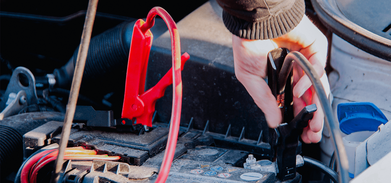 Image of a man's hand in the process of jump-starting a car using jumper cables.