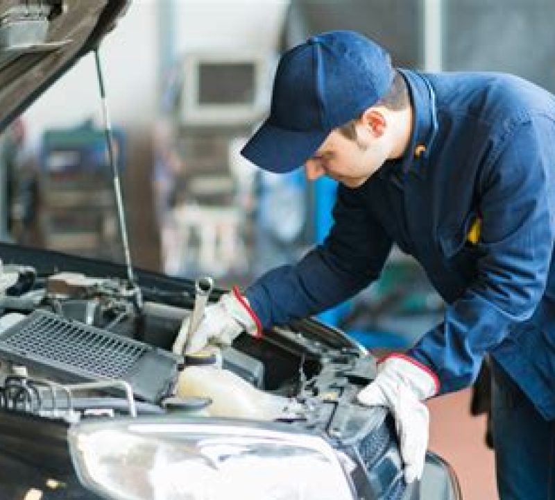 Burt Brothers technician with wrench inspecting under a car's hood.